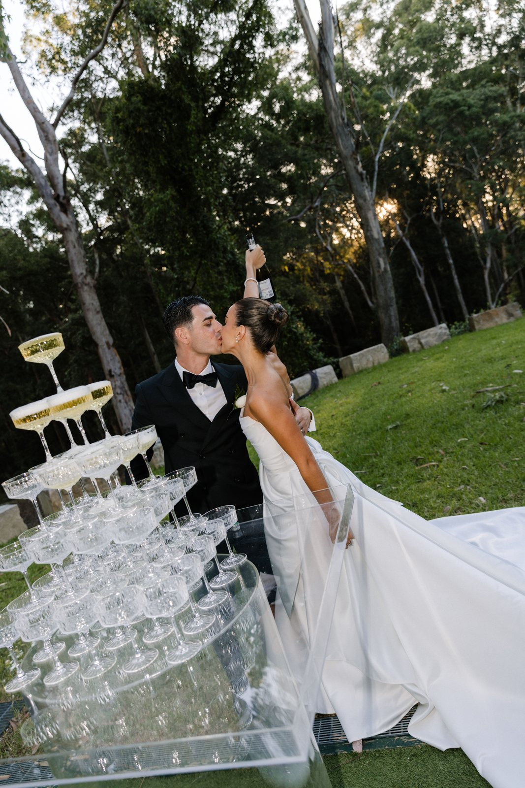 A couple kissing beside a champagne tower on the garden lawn