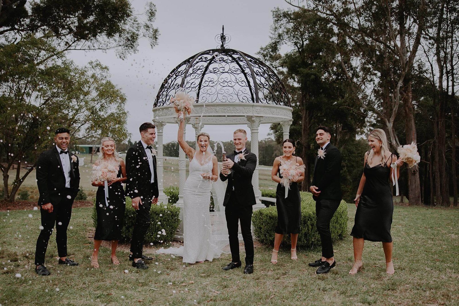 The bridal party cheering in front of the white gazebo