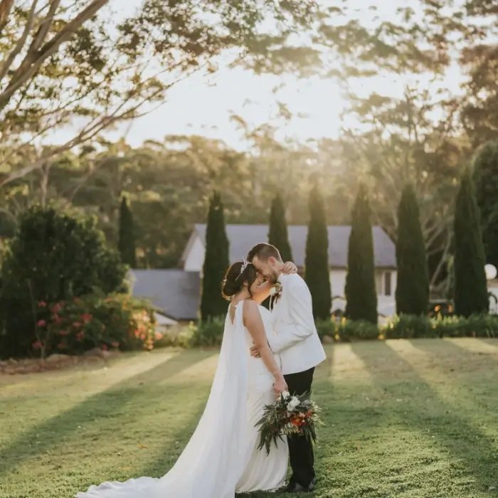 A couple embracing on the lawn in golden light, cypress trees behind