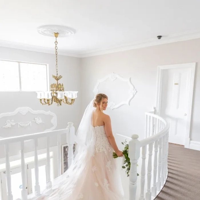 A bride on the curved white staircase inside The Manor