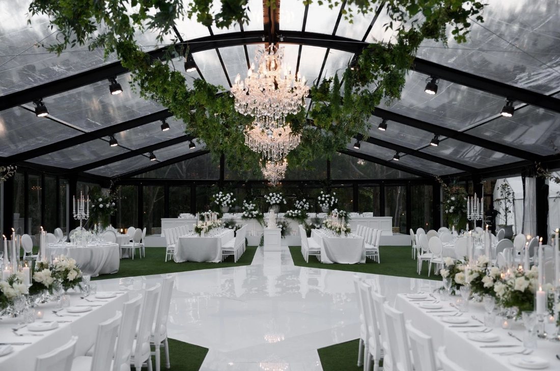 The Pavilion set for a reception with round tables under a chandelier and hanging greenery