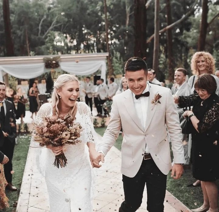 A couple laughing down the aisle as guests throw petals