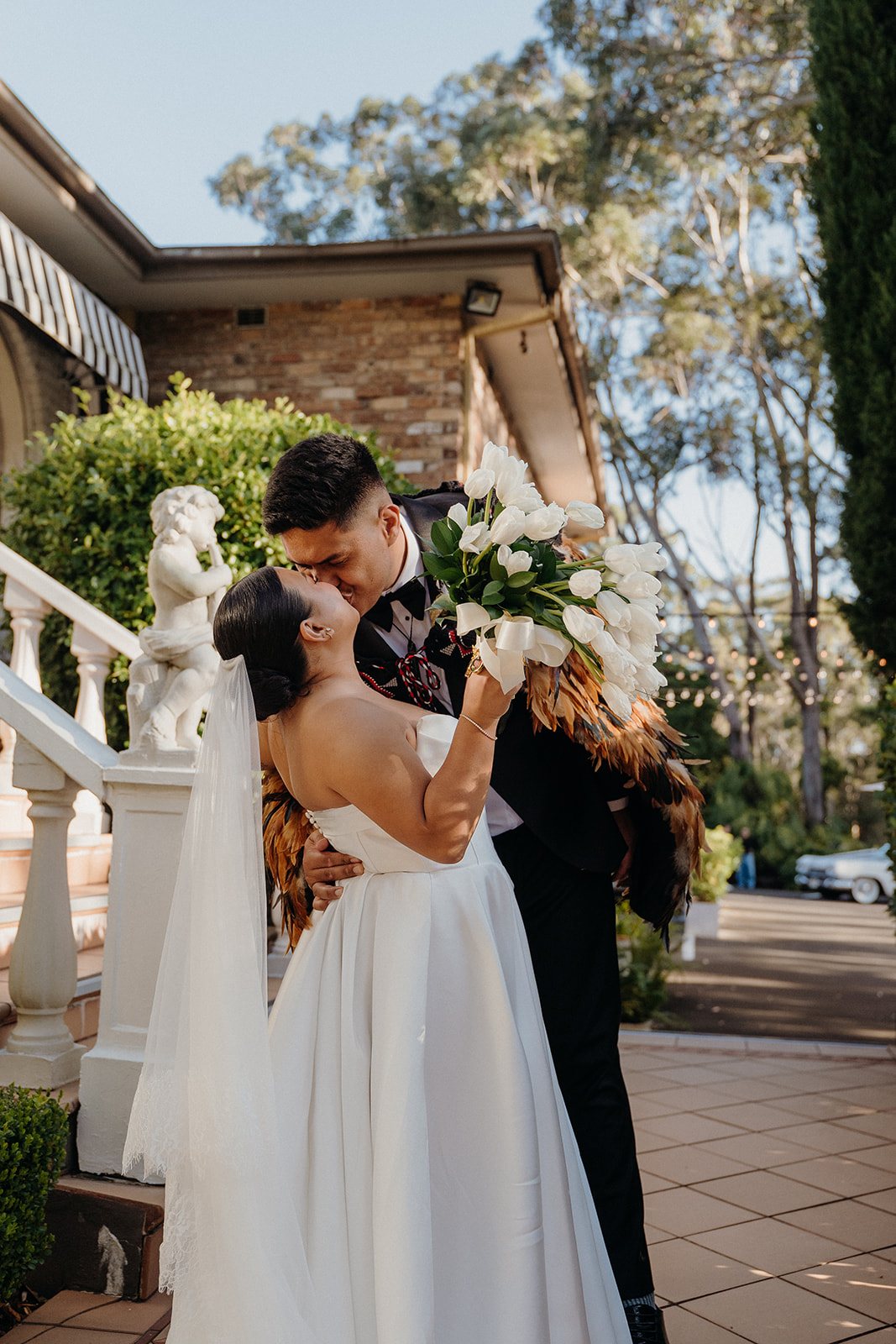 A couple kissing on the white stone staircase outside The Manor